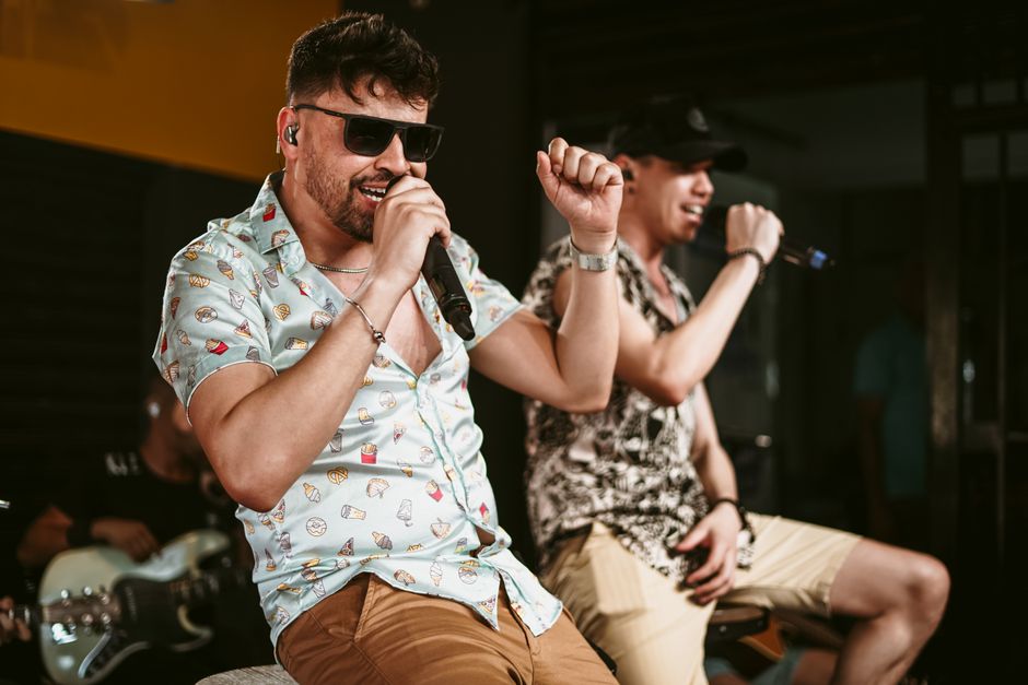 Two male musicians energetically performing with microphones and guitars on stage.