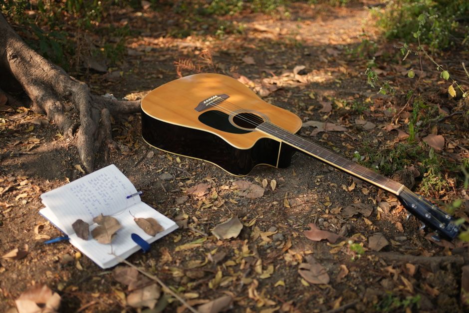 An acoustic guitar rests on forest ground beside an open notebook, capturing the essence of music creation in nature.